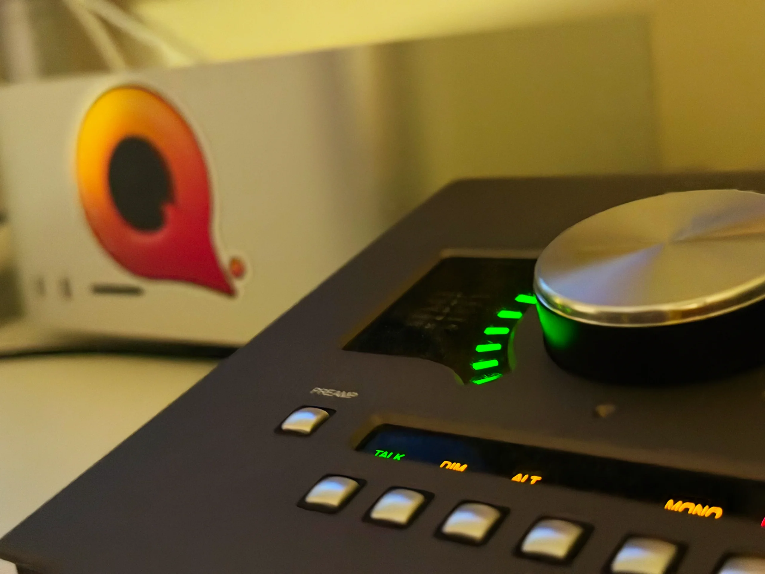 A Universal Audio interface in the foreground with a Mac Studio in the background with a "Q" sticker on the front.